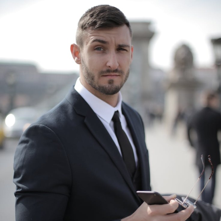 man in black suit holding smartphone and sunglasses